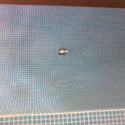 Wnętrze wanny wyłożone drobną, błękitną mozaiką z białymi fugami, widoczny otwór odpływowy i bateria wannowa.